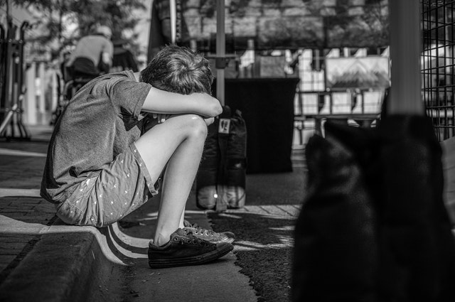 Schwarzweiss Foto von Person die auf der Bordsteinkante sitzt.